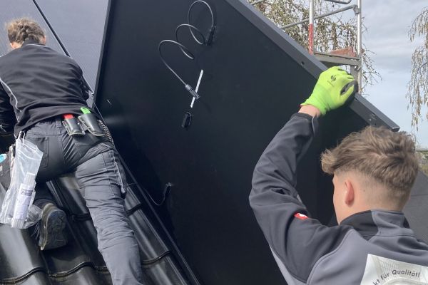 Dachdecker und Dachdeckerin installieren PV-Anlage auf einem Steildach